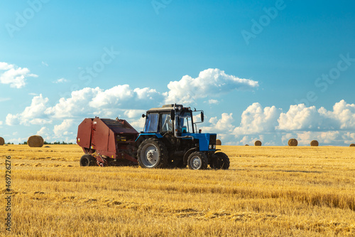 Tractor with bale machine for harvesting straw in the field and making large round bales. Agricultural work  harvesting hay on the hills in summer field