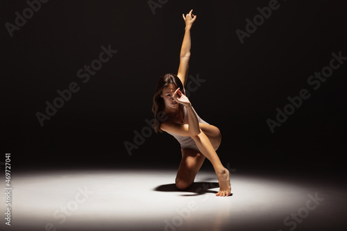 Fotografia Dynamic portrait of young flexible contemp dancer dancing isolated on dark studio background in spotlight