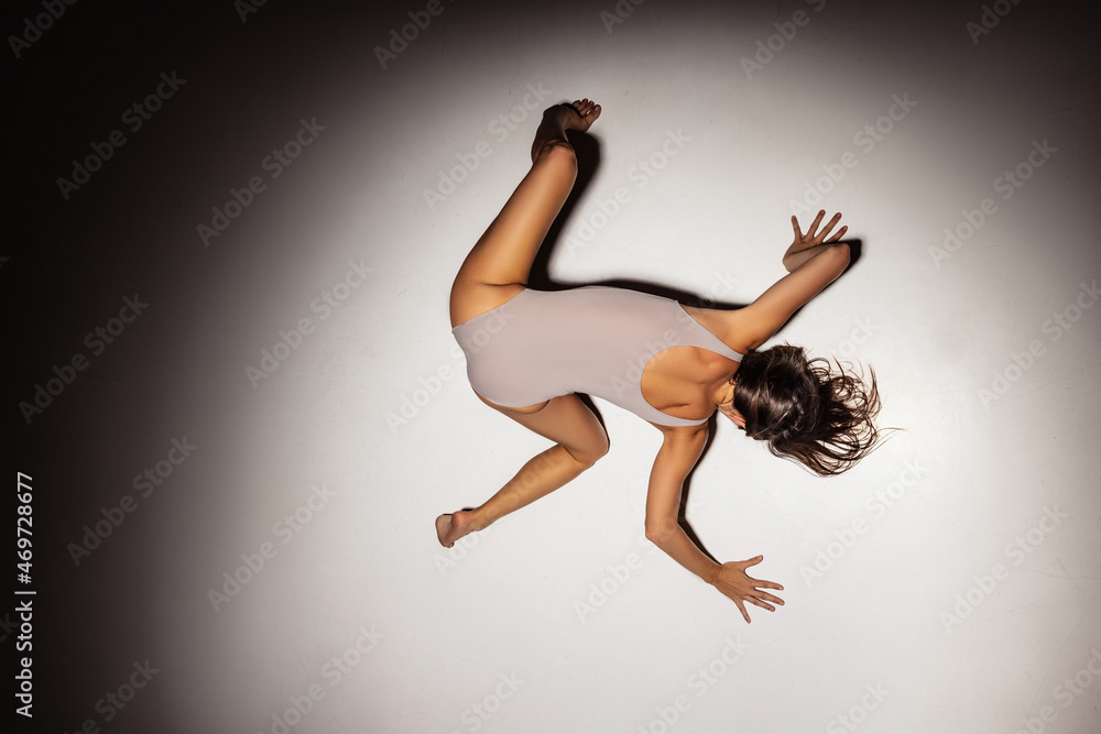 High angle view of young flexible, graceful girl, female contemp dancer in art performance isolated on dark studio background in spotlight.