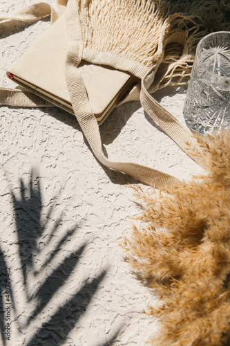 Summer flat lay on a concrete background. Notepad, peaches and an eco-friendly mesh shopping bag. Shadow and sunshine, sun. Summer travel fashion concept. 