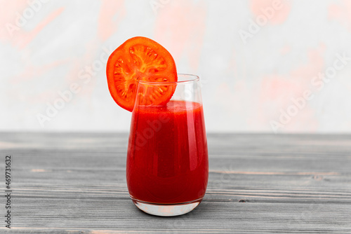 a glass of tomato juice stands on a table made of gray boards on a light background
