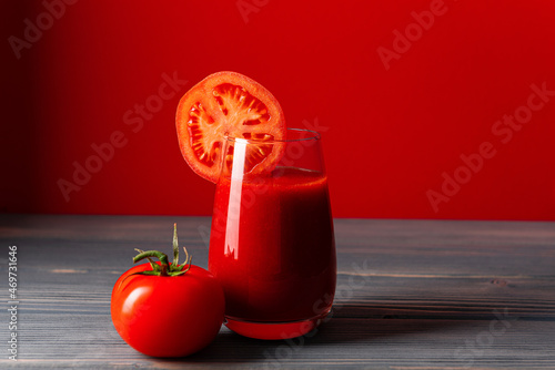 Tomato juice and a whole tomato on a table made of boards on a red background