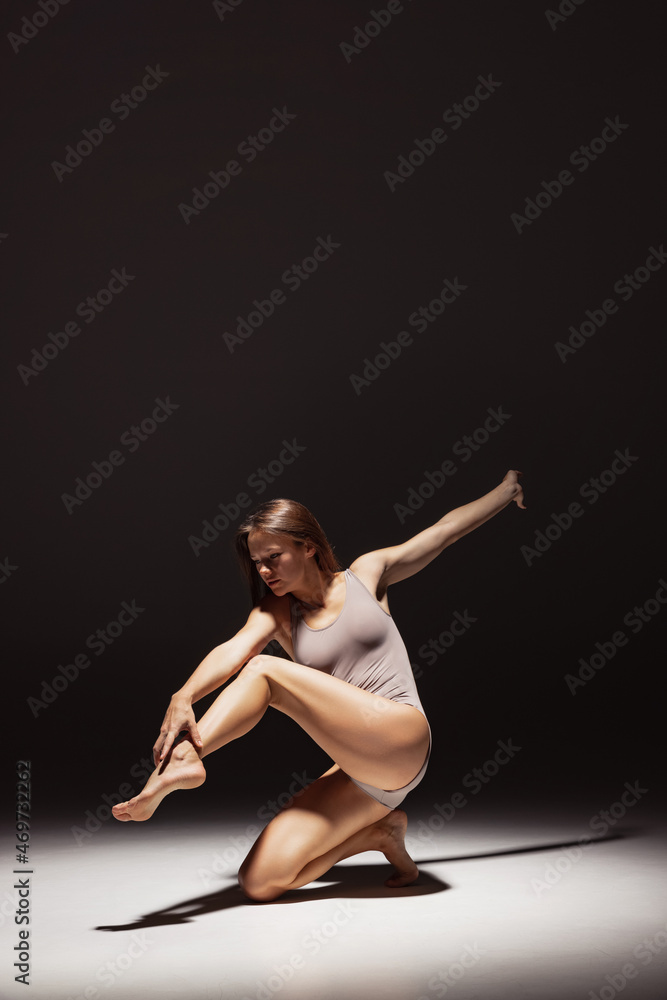 Dynamic portrait of young flexible contemp dancer dancing isolated on dark studio background in spotlight. Art, beauty, inspiration concept. Dynamic portrait of young flexible contemp dancer dancing isolated on dark studio background in spotlight. Art, beauty, inspiration concept.