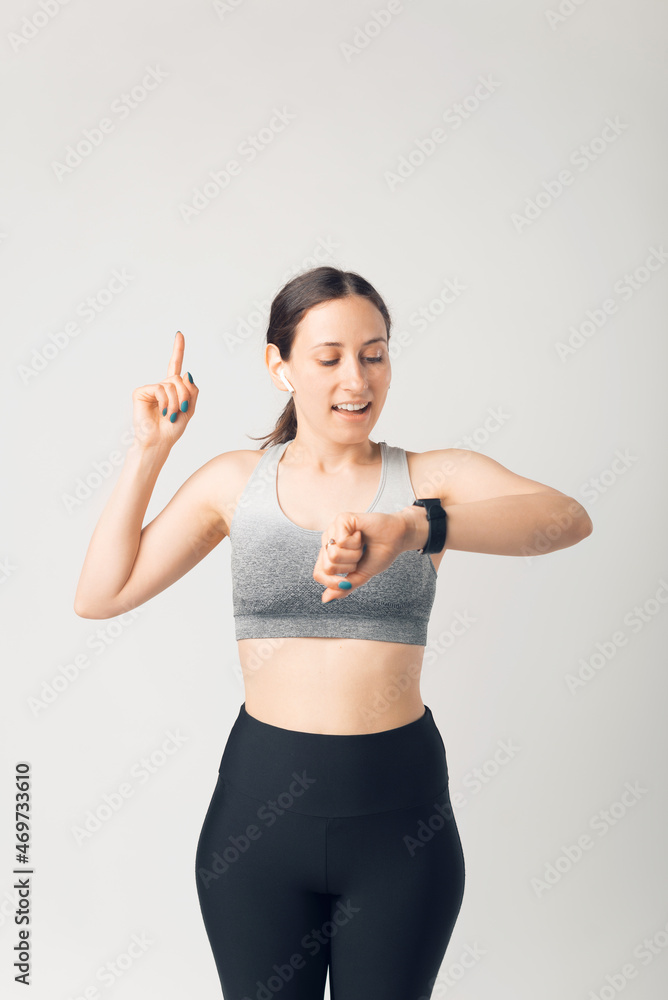 Sporty young woman looking at smartwatch and pointing up, over white background Sporty young woman looking at smartwatch and pointing up, over white background