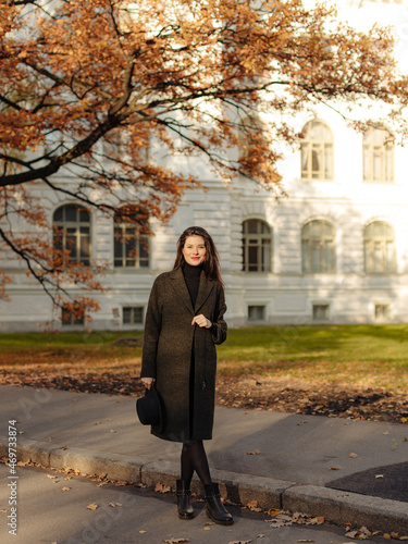 Young beautiful pregnant woman with dark hair in a black tight dress and coat posing on an autumn meadow in the park