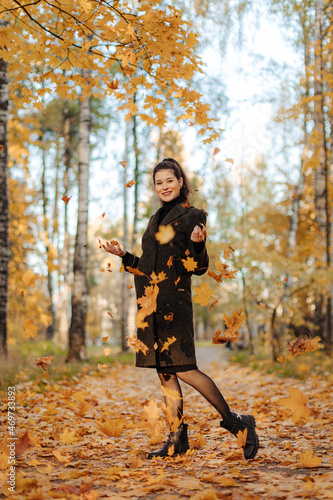 Young beautiful pregnant woman with dark hair in a black tight dress and coat posing on an autumn meadow in the park © cmirnovalexander