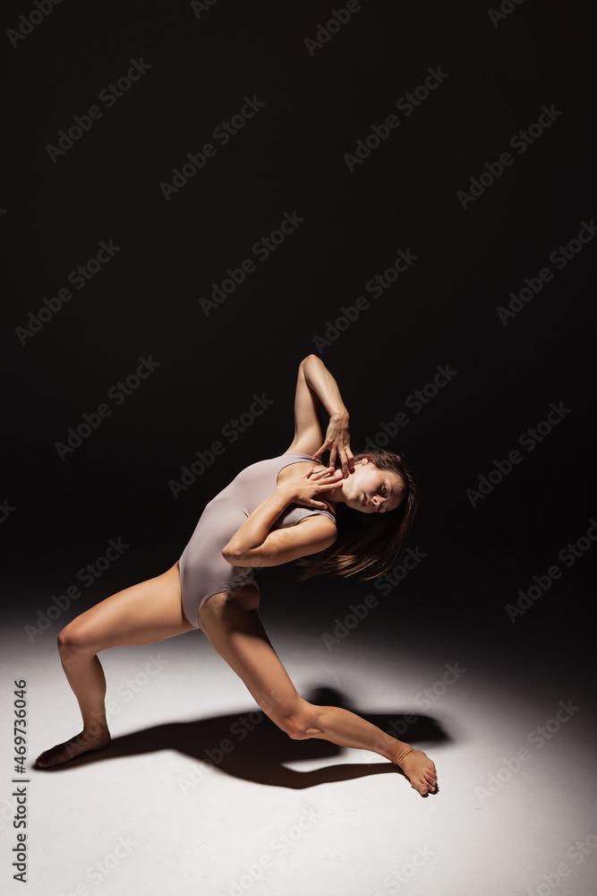 Dynamic portrait of young flexible contemp dancer dancing isolated on dark studio background in spotlight. Art, beauty, inspiration concept. Dynamic portrait of young flexible contemp dancer dancing isolated on dark studio background in spotlight. Art, beauty, inspiration concept.