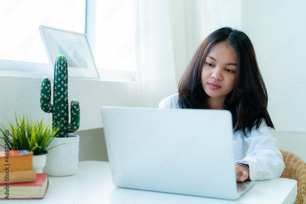 Portrait Cute Asian teen with long hair Wearing a white shirt, sitting online studying with a laptop on the bedroom table with a thoughtful face. Portrait Cute Asian teen with long hair Wearing a white shirt, sitting online studying with a laptop on the bedroom table with a thoughtful face.