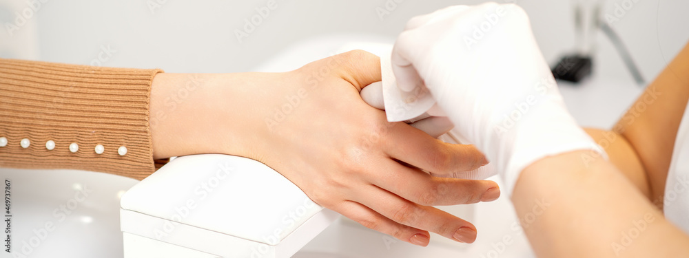 Obraz premium Hands of a manicurist in white protective gloves wipe female nails with a paper napkin in the salon