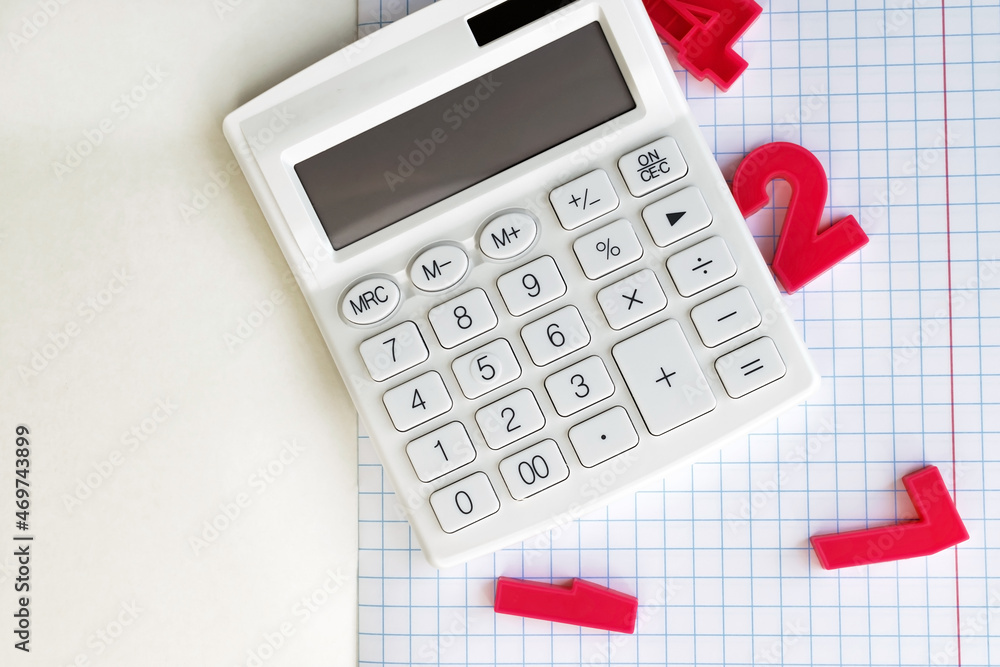 On an open squared notebook is a white calculator and red plastic numbers. Educational and business concept On an open squared notebook is a white calculator and red plastic numbers. Educational and business concept