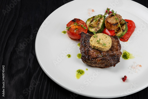 Grilled black angus strip loin steak with vegetables on white plate on black wooden background