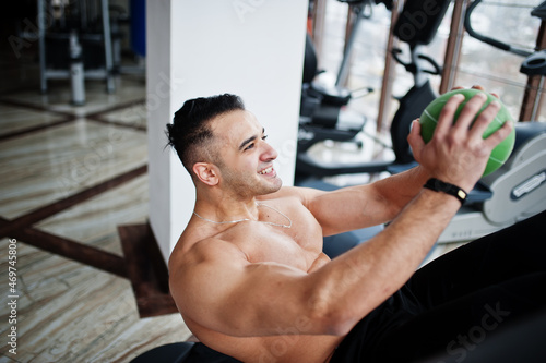 Muscular arab man training in modern gym. Fitness arabian men with naked torso doing exercises with ball.