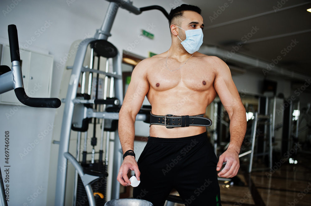Fototapeta premium Muscular arab man, wear medical face mask training in modern gym. Fitness arabian men with naked torso doing exercises, durig coronavirus pandemic.