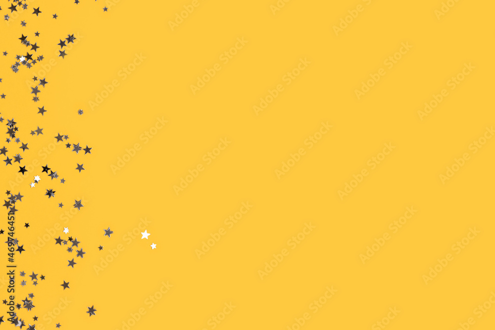 Glowing silver glittering stars confetti scattered on a yellow background with copyspace.