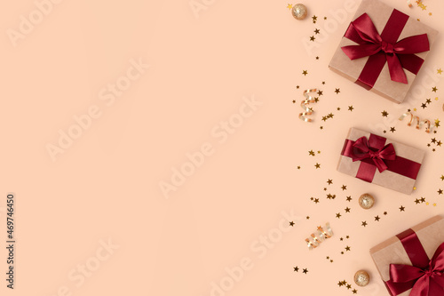 Frame made of gift boxes with red ribbons and gold confetti on a beige background.