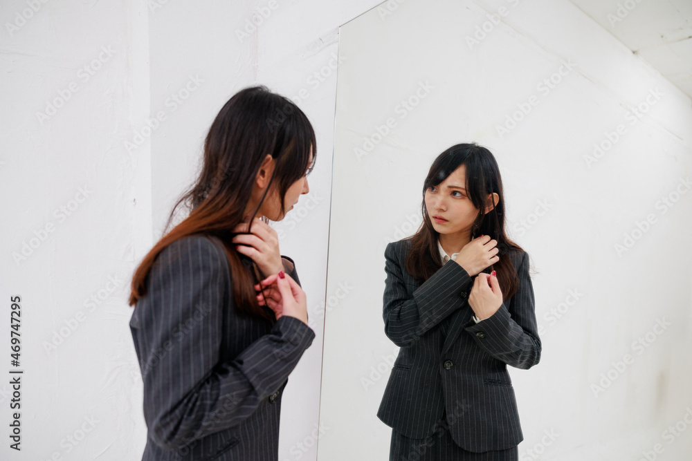 大きな鏡で身だしなみを確認するスーツを着たアジア人女性 大きな鏡で身だしなみを確認するスーツを着たアジア人女性