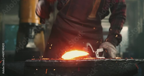 Close-up of blows on hot metal, sparks flying in different directions. The blacksmith holds the workpiece with one hand with tongs, and with the other a hammer with which he forges the product photo
