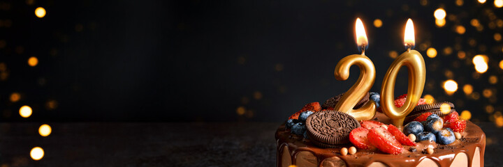 Banner with Chocolate birthday cake with berries, cookies and number twenty golden candles on black background, copy space