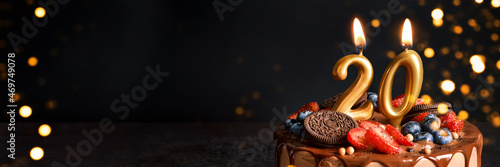 Banner with Chocolate birthday cake with berries, cookies and number twenty golden candles on black background, copy space photo