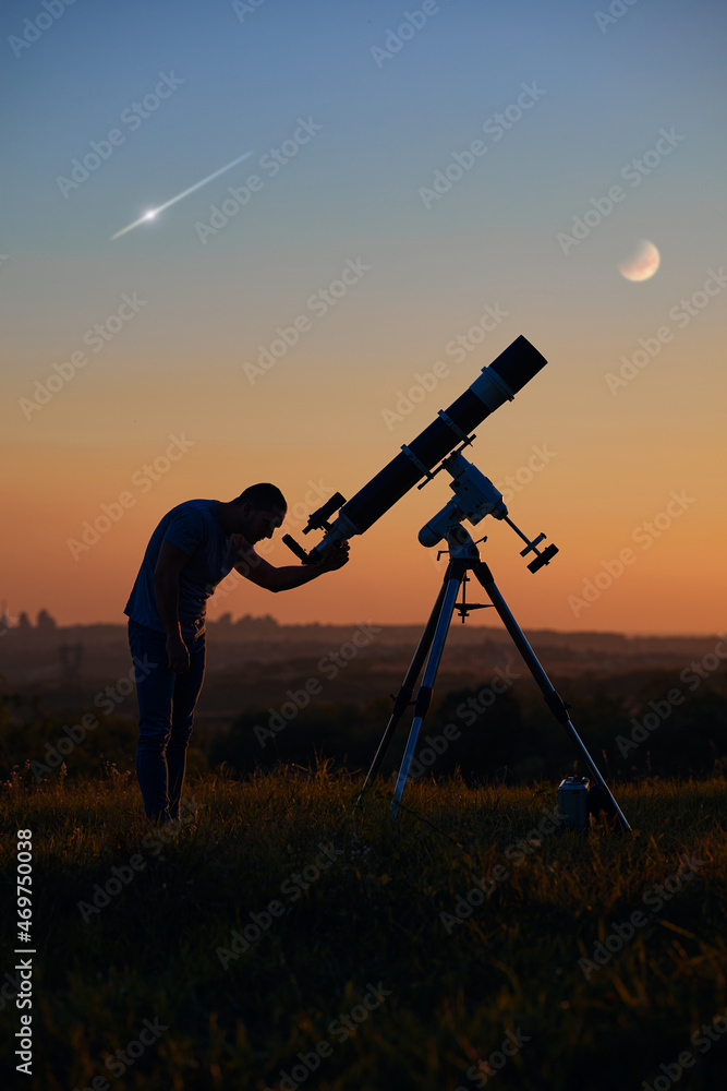 Silhouette of a man, astronomical telescope, countryside, lunar eclipse and meteor shower.