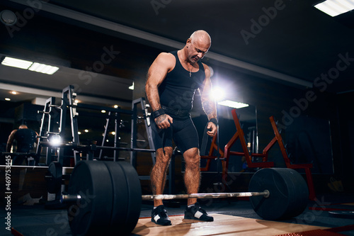 Older powerlifter preparing to exercise deadlift with barbell while on cross training in a gym. photo
