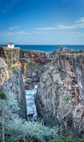 The cave, the old house and the stone bridge of the Hell's Mouth (Boca Do Inferno) seeing from a different angle while people are visiting in Cascais, Lisbon, Portugal. photo