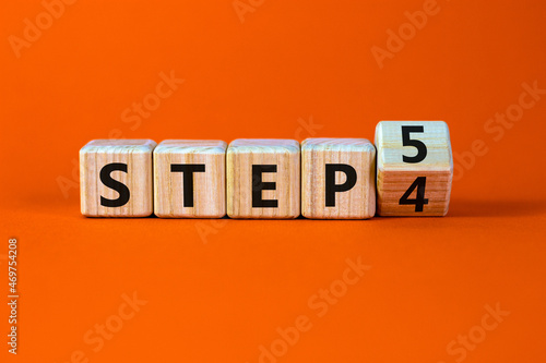 Step 4 or 5 symbol. Turned a wooden cube and changed words Step 4 to Step 5. Beautiful orange table, orange background, copy space. Business and Step 4 or 5 planning concept.