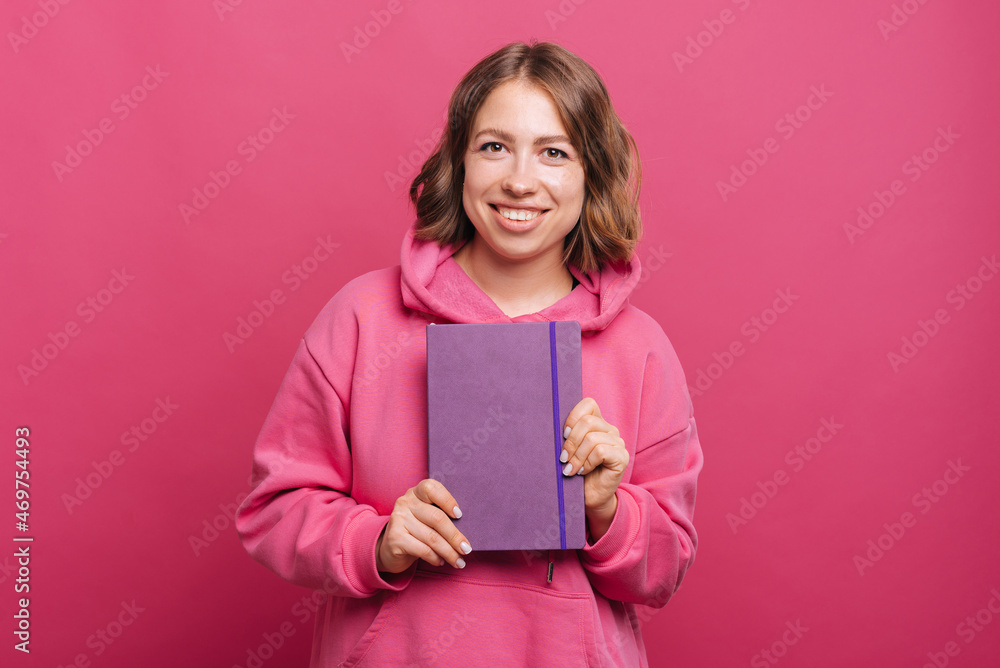 Portrait of young cheerful woman holding agenda planner over pink background. Portrait of young cheerful woman holding agenda planner over pink background.