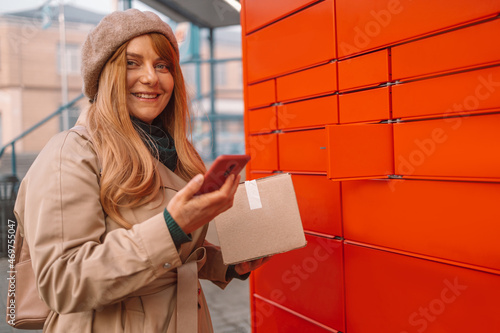 Woman holding smartphone using automated self service post terminal machine or locker to deposit the parcel for storage photo