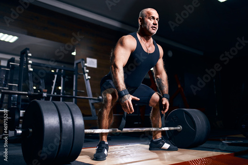 Adult bald male powerlifter bodybuilder preparing deadlift barbell in gym. Powerlifting Bodybuilding