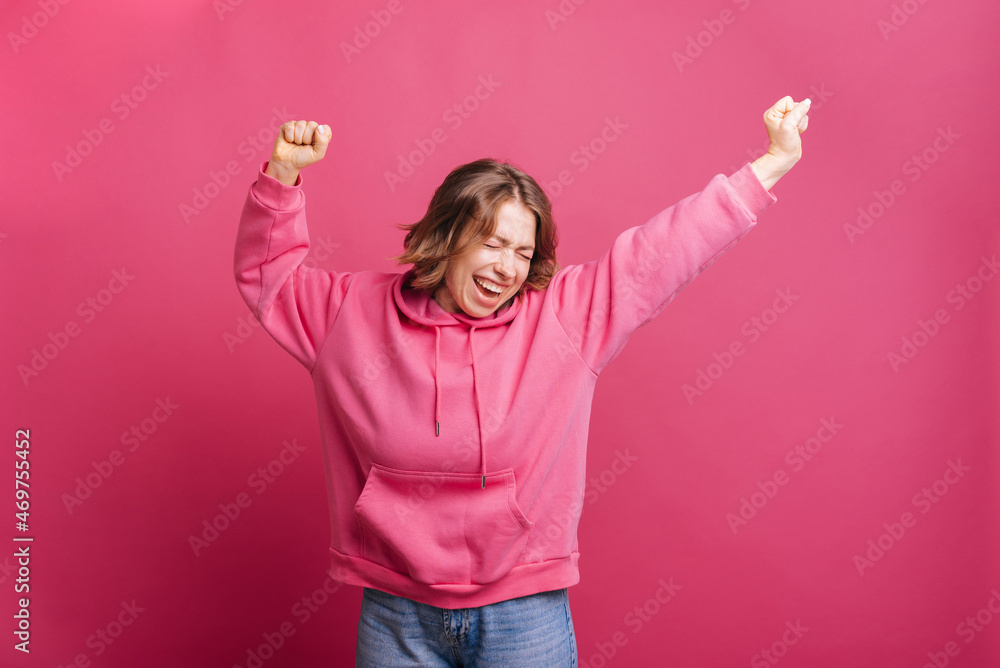 Amazed young trendy woman in pink hoodie jumping and celebrating over pink background. Amazed young trendy woman in pink hoodie jumping and celebrating over pink background.