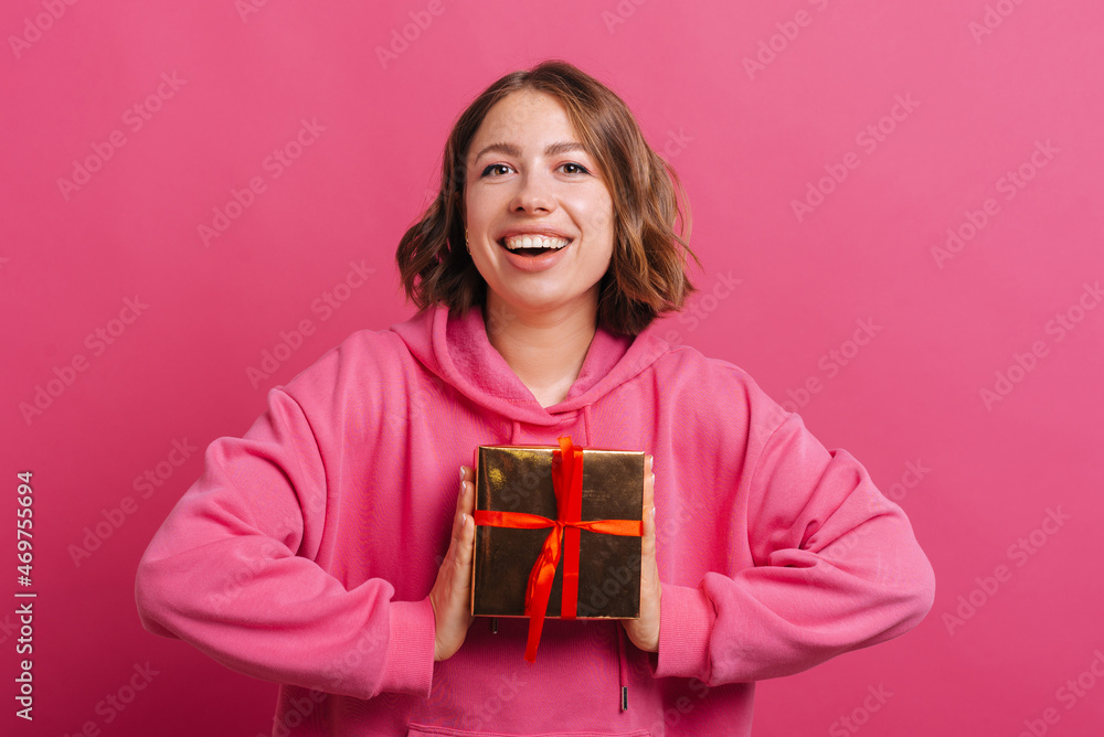 Excited young smiling woman holding her gift for xmas over pink background. Excited young smiling woman holding her gift for xmas over pink background.