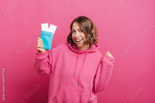 Happy woman holding passport with airplane tickets over pink background.