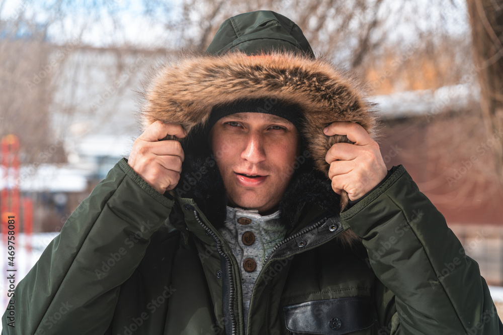 A man in a winter jacket with a hood against the background of a snow-covered city A man in a winter jacket with a hood against the background of a snow-covered city