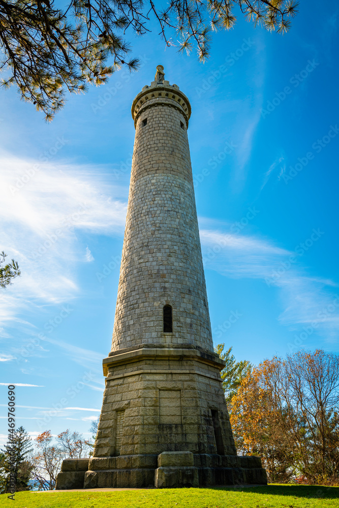 Myles Standish Monument and surrounding settings with trees and clouds on blue sky background.