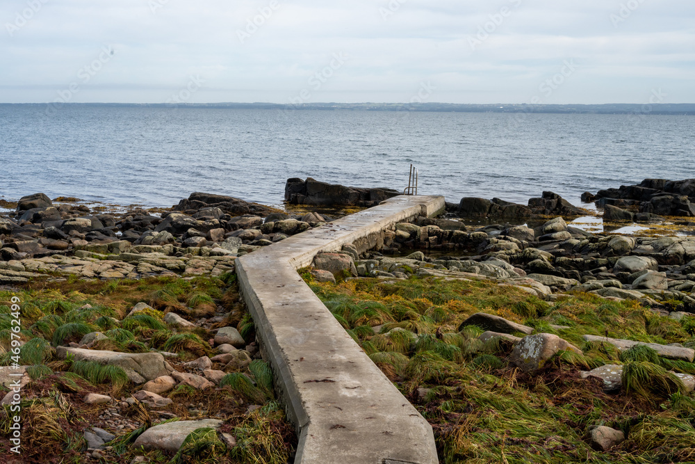 Rocky shoreline with a concrete jetty. Blue water and a blu sky in the background. Picture from Skalderviken, southern Sweden Rocky shoreline with a concrete jetty. Blue water and a blu sky in the background. Picture from Skalderviken, southern Sweden