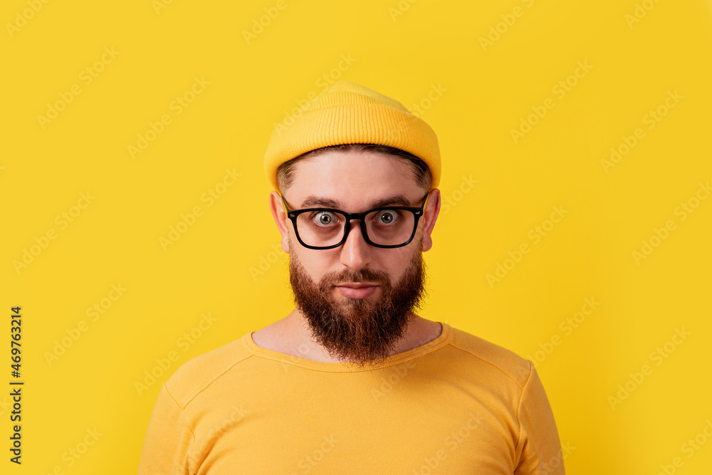 man with crazy look over yellow background, bearded guy looking into camera