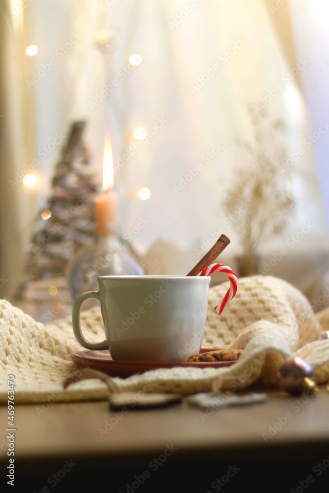 Cup of warm drink with candy cane and cinnamon stick, soft blanket and various Christmas decorations. Hygge at home. Selective focus. Cup of warm drink with candy cane and cinnamon stick, soft blanket and various Christmas decorations. Hygge at home. Selective focus.