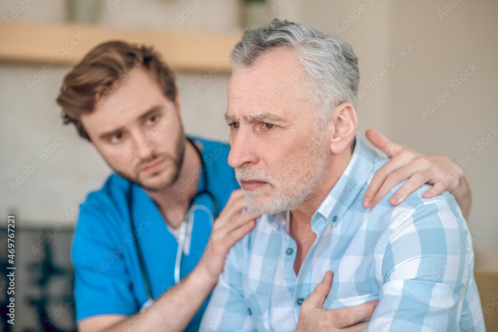 Attentive cardiologist supporting a frightened sick man Attentive cardiologist supporting a frightened sick man