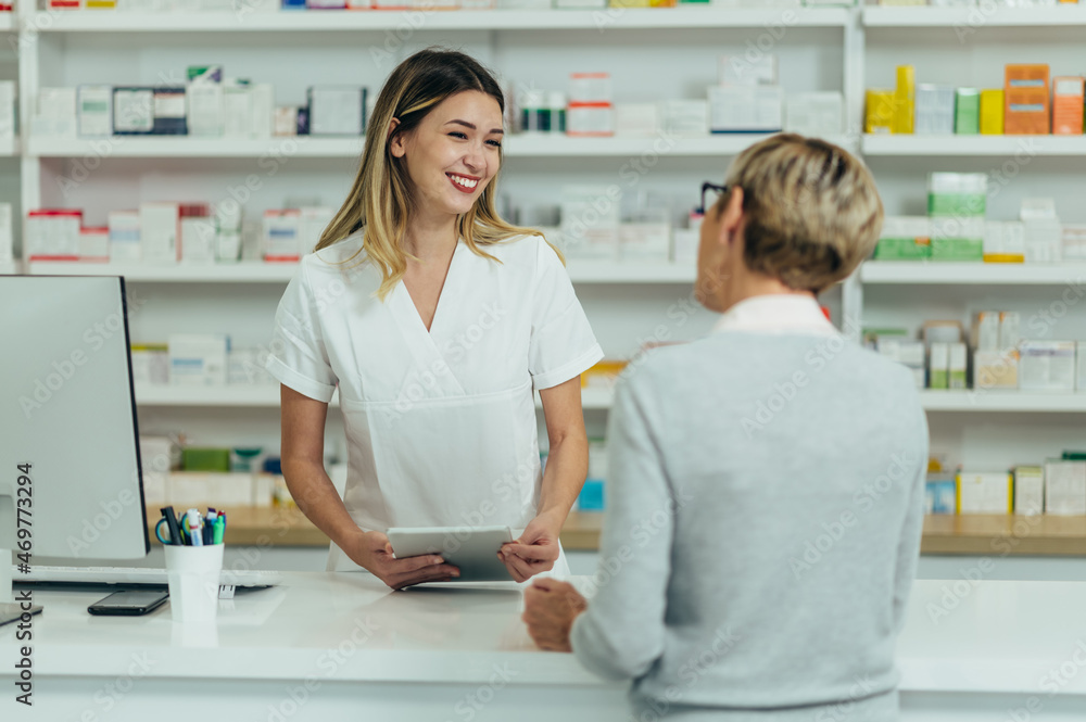 Fototapeta premium Male pharmacist selling medications at drugstore to a senior woman customer