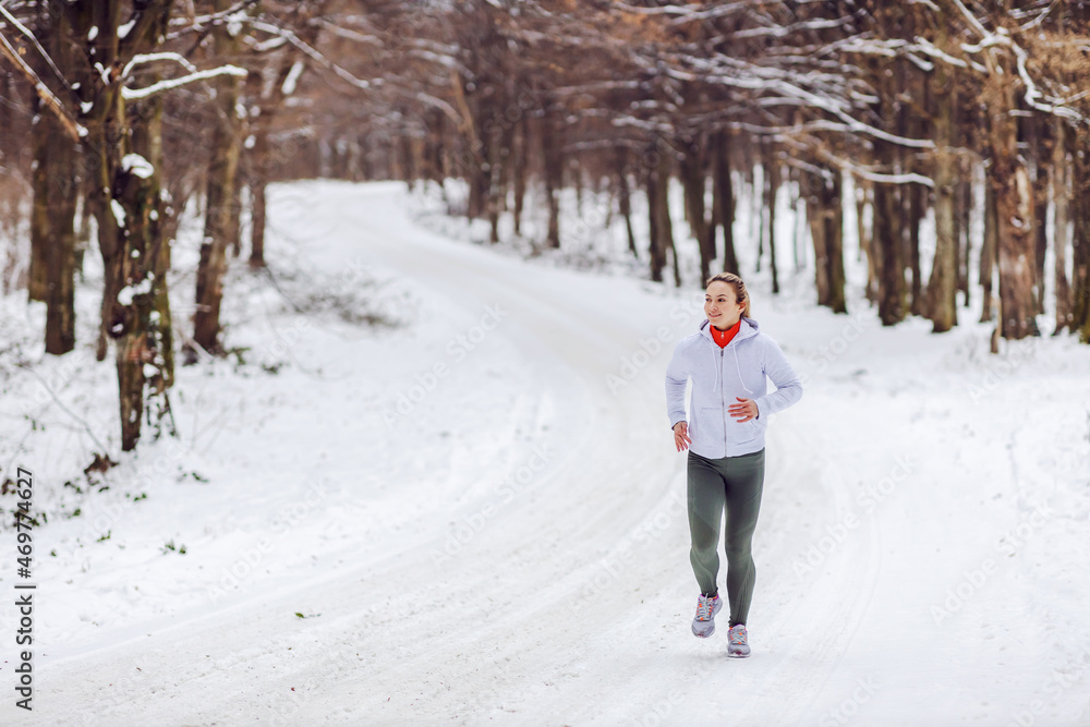 Fit sportswoman running in nature on a snowy winter day. Cold weather, snow, healthy life, fitness, nature