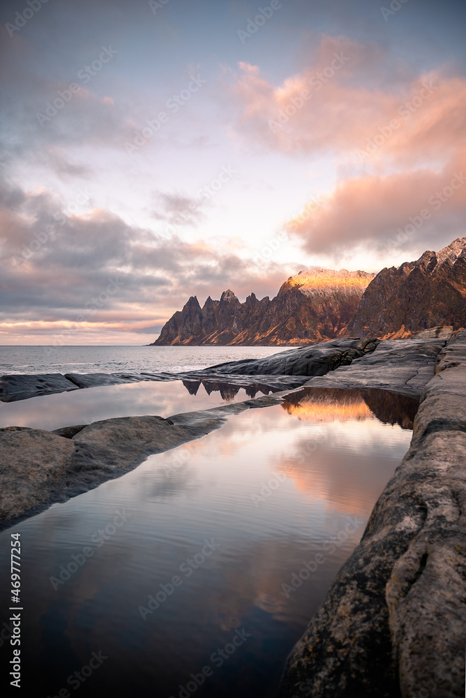 Tugeneset viewpoint in Senja, Norway at sunset with reflections of the mountains and the landscape in the calm water among the cliffs
