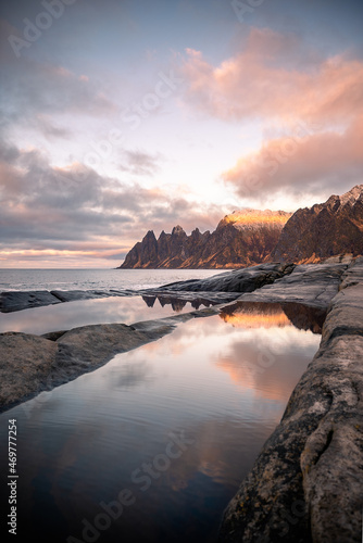 Tugeneset viewpoint in Senja, Norway at sunset with reflections of the mountains and the landscape in the calm water among the cliffs