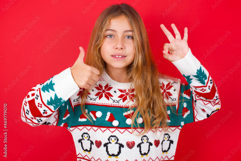 little kid girl wearing knitted sweater christmas over red background smiling and looking happy, carefree and positive, gesturing victory or peace with one hand little kid girl wearing knitted sweater christmas over red background smiling and looking happy, carefree and positive, gesturing victory or peace with one hand