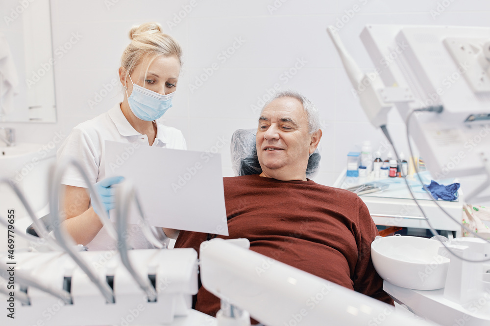 Obraz premium Woman doctor dentist works with an elderly man in a dental chair treats teeth and shows x-rays