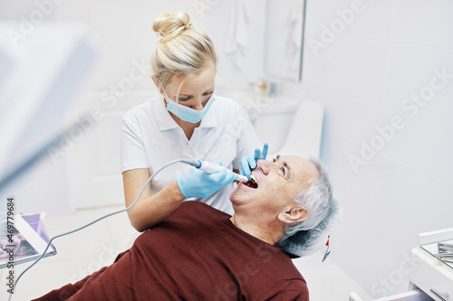 Woman doctor dentist works with an elderly man in a dental chair treats teeth and shows x-rays