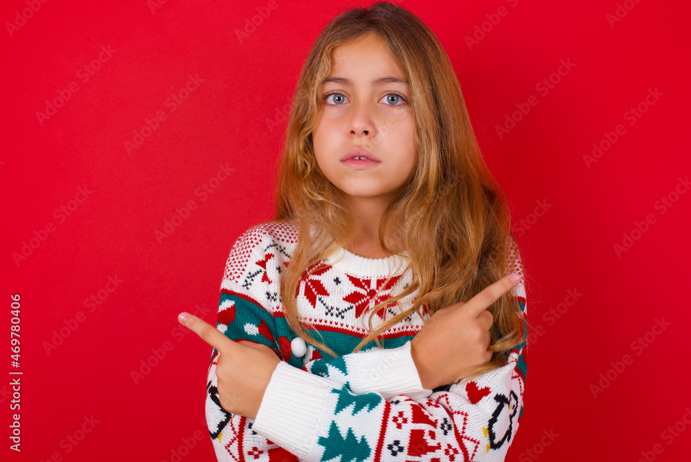 Serious little kid girl wearing knitted sweater christmas over red background crosses hands and points at different sides hesitates between two items. Hard decision concept Serious little kid girl wearing knitted sweater christmas over red background crosses hands and points at different sides hesitates between two items. Hard decision concept