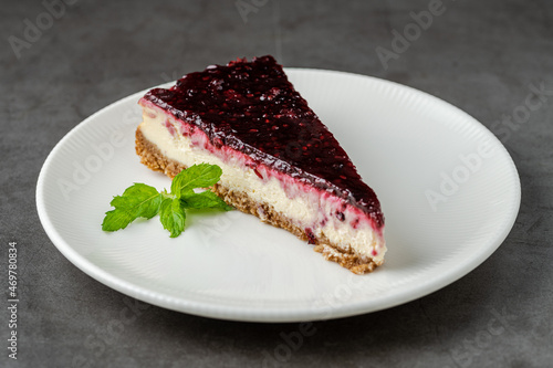 Raspberry cheesecake on white plate on dark stone table