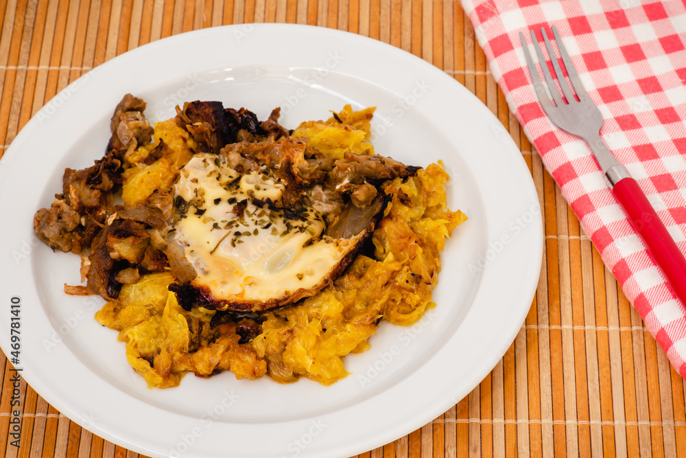 Plato de berenjenas con naranja y miel, un huevo frito encima, una servilleta a cuadros y un tenedor rojo Plato de berenjenas con naranja y miel, un huevo frito encima, una servilleta a cuadros y un tenedor rojo