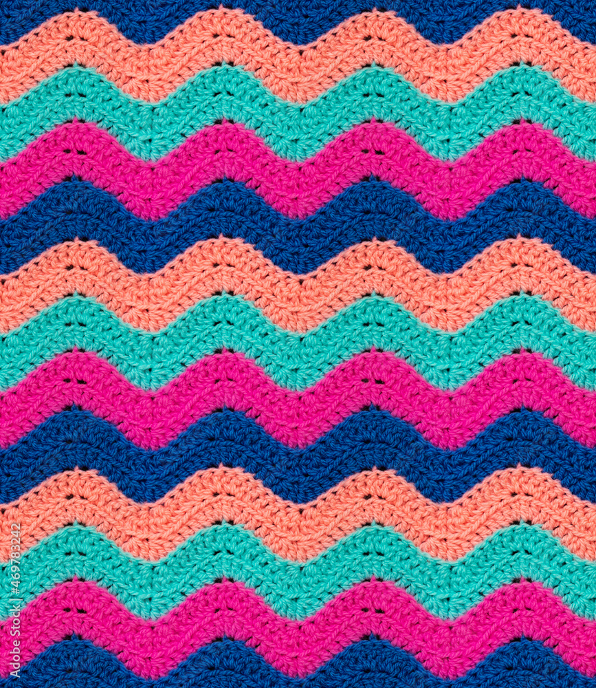Seamless knitted pattern in the form of zigzags is crocheted with multi-colored threads. Acrylic baby yarn. Colorful background.